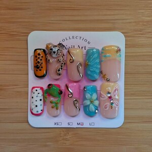 May include: A set of ten press-on nails on a white display card labeled Collection Nail Art. The nails feature diverse designs including a leopard, a green frog, a blue flower, a butterfly, and various patterns in orange, pink, and blue colors.