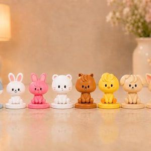 May include: A set of eight small, stylised animal figurines arranged in a row. The figures include a grey wolf, white rabbit, pink rabbit, white cat, brown squirrel, yellow chick, beige puppy, and a tan fox, each on a circular base.