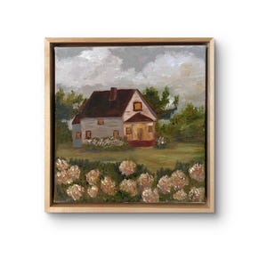 Può includere: Un dipinto a olio quadrato in una cornice di legno chiaro che raffigura una casa a due piani con tetto scuro e veranda. La casa è circondata da alberi verdi e da un campo di fiori bianchi sotto un cielo grigio nuvoloso.