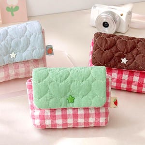 May include: Three small quilted pouches with flap closures. One pouch has a light blue heart-quilted flap and pink gingham body, one has a mint green heart-quilted flap and pink gingham body, and one has a brown heart-quilted flap and red gingham body.