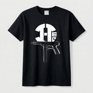 May include: A black short-sleeve t-shirt featuring a white graphic print on the chest. The design includes a stylized circular logo with the letters H and E, positioned above a detailed black and white illustration of a submachine gun.