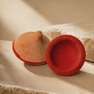 May include: Two circular terracotta objects with a matte finish. One object is a dome shape with a pointed top and a red base, while the other is a flat, circular disc with a vibrant red surface. Both items feature a natural, earthy texture.
