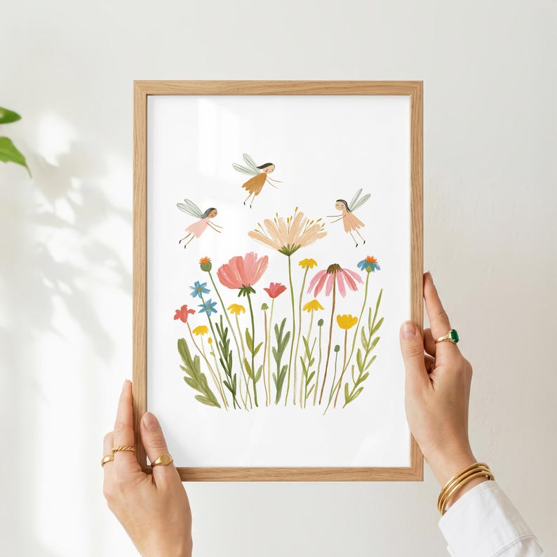 May include: A framed art print featuring a white background with a colorful illustration of various wildflowers in shades of pink, yellow, and blue, accompanied by three small winged fairy figures flying above the stems in a light, whimsical style.