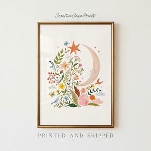 May include: A framed art print titled Creative Casa Prints featuring a crescent moon with a face surrounded by colorful wildflowers, green foliage, a star, small birds, butterflies, and tiny hearts on a cream background with text below.