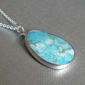 May include: A silver necklace featuring a pendant with a teardrop-shaped turquoise stone. The stone has a light blue color with white and green veining. The pendant is set in a silver bezel and hangs from a delicate silver chain.