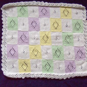 Può includere: Una copertina per neonati in crochet bianco con un motivo a scacchi in verde pastello, giallo e viola. La copertina ha un delicato bordo in crochet.