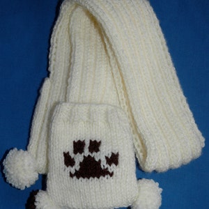 May include: White knitted scarf with a brown paw print design and white pom-poms on the ends.