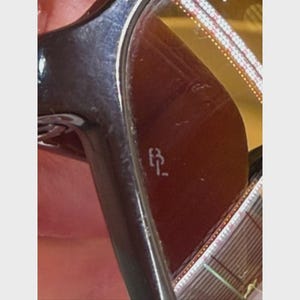 Puede incluir: Un par de gafas de sol de color marr&oacute;n oscuro con un acabado brillante en la montura. La lente muestra un peque&ntilde;o logotipo grabado en blanco que consiste en las letras BL. La superficie de la lente muestra el reflejo de una cuadr&iacute;cula.