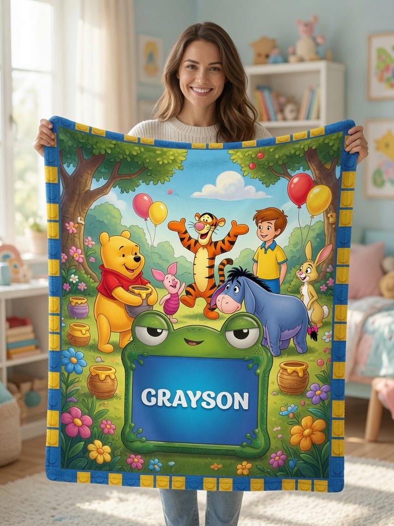 Op de afbeelding: Een zachte fleece deken met een kleurrijke illustratie van Winnie de Poeh, Teigetje, Knorretje, Iejoor, Konijn en Janneman Robinson in een bos. Een groot groen kikker-vormig kader op de voorgrond toont de naam GRAYSON.