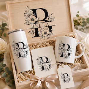 May include: A light-colored wooden gift box containing a white stainless steel tumbler, a white ceramic mug, a rectangular card, and a gift tag. Each item features a black floral design with the letter B and the name BELLA printed in the center.