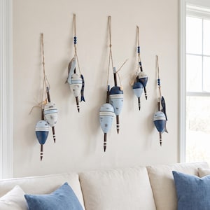 May include: Five wall-mounted hanging decorations featuring wooden fishing floats in shades of navy blue, light blue, and white. Each piece is suspended by twine with small blue beads and includes attached wooden fish or shell accents.