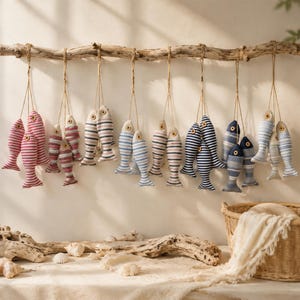 Pode incluir: Uma coleção de ornamentos de peixe em tecido pendurados num pedaço horizontal de madeira flutuante. Cada peixe apresenta riscas horizontais em tons de vermelho, azul e cinzento, com um pequeno olho feito de um botão de madeira.