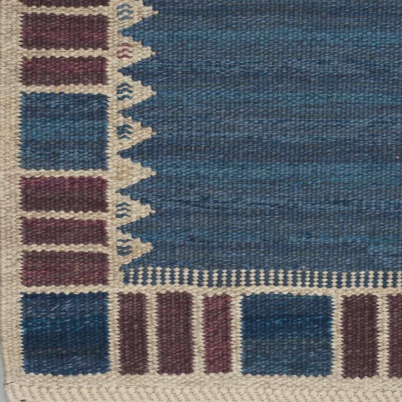 May include: A woven rug featuring a large solid blue central field bordered by a geometric pattern of alternating dark blue and deep maroon rectangular blocks separated by thin cream-colored lines and a jagged sawtooth edge.