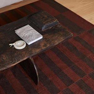 Peut inclure: Une table basse en bois brun foncé avec un bord naturel, dotée d'un plateau rectangulaire et d'une base de support incurvée. Un livre avec le mot SLOW sur la couverture et un petit plat rond en céramique blanc cassé contenant des herbes séchées.