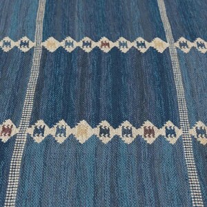 May include: A woven rug featuring a deep blue and teal gradient background with vertical white checkered stripes. Horizontal bands of repeating diamond-shaped motifs in white, tan, and dark brown are spaced evenly across the textured surface.
