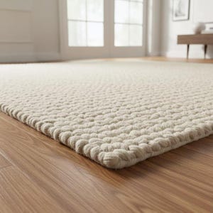 May include: A rectangular area rug featuring a thick, chunky knit texture in a solid off-white color. The rug is constructed from interconnected, rounded loops of yarn, creating a dense, tactile surface that covers the floor space.