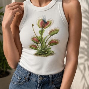 Puede incluir: Una camiseta de tirantes blanca acanalada con una ilustración botánica detallada de una planta Venus atrapamoscas con hojas verdes, trampas teñidas de rojo y un pequeño insecto azul posado en una de las trampas abiertas, centrada en el frente.