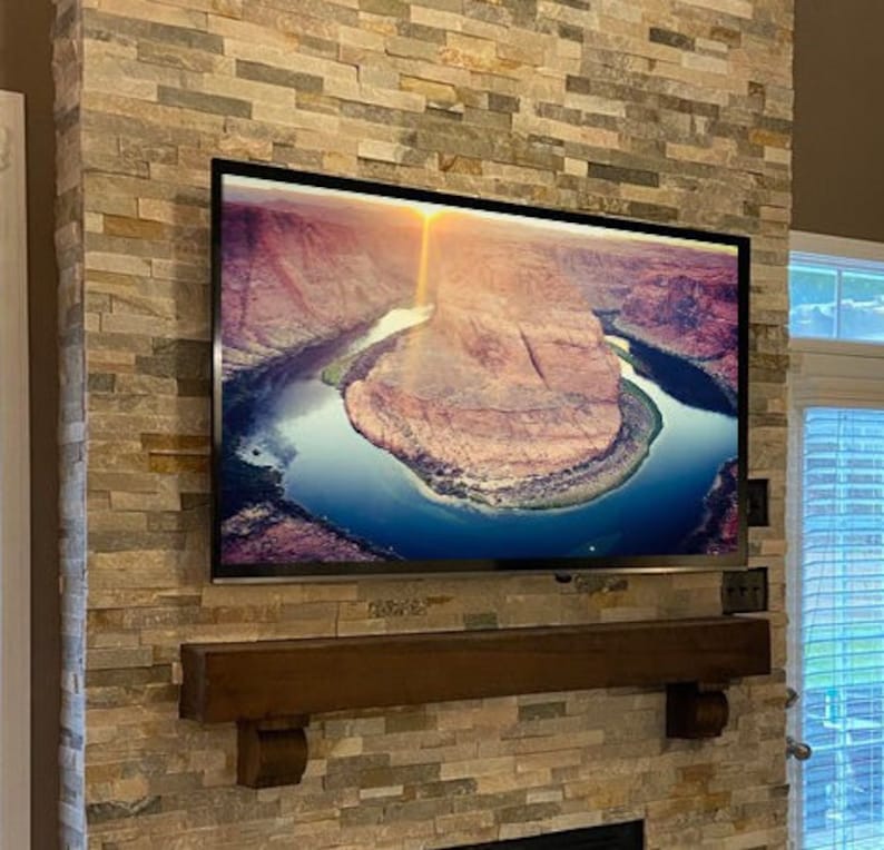 May include: A large flat-screen television mounted on a stone fireplace. The screen displays a scenic view of a river winding through a canyon. A dark wooden mantel is below the TV.