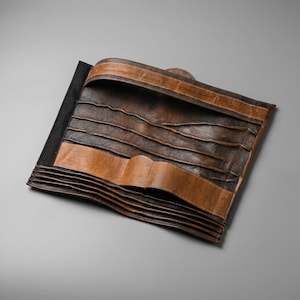 Puede incluir: Un organizador rectangular de cuero marr&oacute;n con m&uacute;ltiples ranuras y bolsillos horizontales. El art&iacute;culo presenta un dise&ntilde;o bicolor con secciones texturizadas en marr&oacute;n oscuro y detalles de cuero color canela en los bordes y divisores.