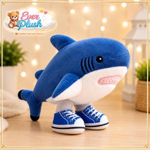 May include: A plush shark toy with a deep blue upper body and a white underbelly. The shark features black eyes, stitched gill slits, and a light pink mouth with visible teeth. It is wearing a pair of blue and white canvas sneakers on its feet.