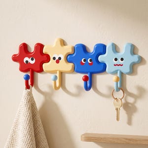 May include: A wall-mounted rack featuring four puzzle-piece shaped hooks in red, cream, blue, and light blue. Each piece has a cartoon face with eyes and a mouth. A beige textured cloth hangs from the red hook, and a metal key hangs from the light blue hook.