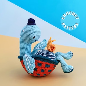 May include: A light blue crocheted turtle with a dark blue hat, sitting in a red and dark blue woven shell, holding a small orange snail. The text CROCHET PATTERN is visible in a blue circle in the upper right corner of the image.
