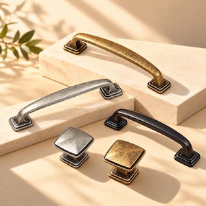 May include: A collection of cabinet hardware including three arched metal pulls and two square knobs. The hardware features antique brass, brushed silver, and matte black finishes, each with a square base and a smooth, curved design.