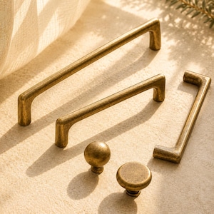 May include: A collection of antique brass hardware including three rectangular drawer pulls with rounded edges and two circular cabinet knobs. Each piece features a weathered, metallic finish with subtle variations in tone and texture.