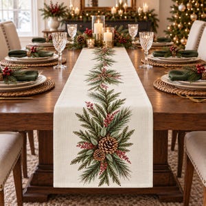 May include: A cream-colored table runner featuring a repeating botanical print of green pine branches, brown pinecones, and clusters of red berries. The runner is centered on a wooden dining table set with plates, napkins, and glassware.