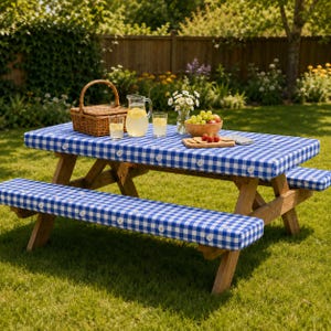 May include: A wooden picnic table with attached benches featuring blue and white gingham cushions with small white daisy accents. On the table sits a woven wicker basket, a glass pitcher of lemonade, two glasses, and a bowl of fresh green grapes.