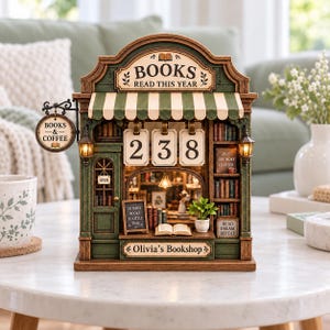 May include: A miniature bookshop model featuring a green and cream striped awning, a hanging sign reading "BOOKS & COFFEE," and a counter with the text "Olivia's Bookshop." The display includes shelves of books, a calendar showing 238, and small lights.