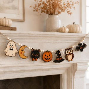 May include: A decorative garland featuring wooden cutouts of a ghost, a crescent moon, a black cat, a jack-o'-lantern, a witch hat, an owl, and a bat, all strung together with natural twine and small white wooden beads in a repeating pattern.