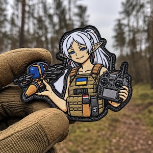 May include: An embroidered patch featuring an anime-style elf character with white hair, wearing a tan tactical vest with a blue and yellow flag patch. The character holds a small drone in one hand and a black remote control in the other.