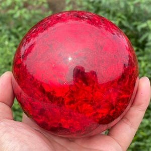Peut inclure: Un objet sphérique lisse d'une couleur rouge translucide profonde avec une texture interne complexe et fracturée. La surface est polie et réfléchissante, montrant des reflets lumineux sur sa forme arrondie, créant un aspect vibrant.