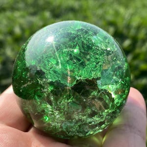 Peut inclure: Un objet sphérique en verre vert transparent présentant une texture interne craquelée ou fracturée. La surface de la sphère est lisse et polie, tandis que l'intérieur révèle un réseau complexe de fissures et d'éclats réfléchissant la lumière.