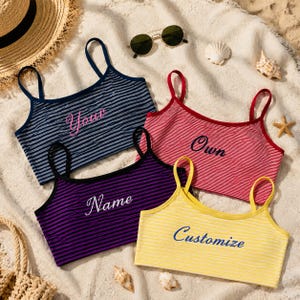 May include: Four sleeveless crop tops with thin straps, each featuring horizontal stripes and embroidered text. The navy top says Your, the red top says Own, the purple top says Name, and the yellow top says Customize in cursive script.