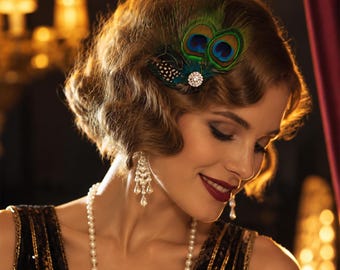 Puede incluir: Un accesorio para el cabello con plumas de pavo real iridiscentes y un adorno central circular de pedrería. La pieza se luce en cabello ondulado, junto con pendientes largos de perlas en varios niveles y un collar de perlas blancas.