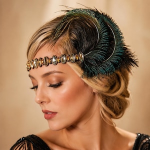 May include: A decorative headband featuring a row of oval-shaped amber-colored crystals set in a dark metal frame. The accessory is adorned with a large, prominent plume of iridescent green and black peacock feathers attached to the side.