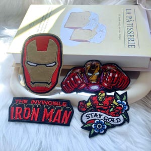 Puede incluir: Cuatro parches bordados con im&aacute;genes de Iron Man. Uno es un casco rojo y dorado, otro muestra a Iron Man volando, uno es un parche rectangular con el texto THE INVINCIBLE IRON MAN y otro muestra a Iron Man con flores y el texto STAY GOLD.