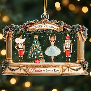 May include: A decorative Christmas ornament featuring a Nutcracker stage scene with a mouse king, a Christmas tree, a ballerina, and a soldier. The top banner reads The Nutcracker 2026 and the base is inscribed with Amelia as Mouse King.