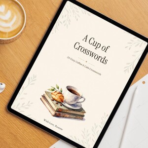 以下が含まれることがあります： A Cup of Crosswords, 25 Cozy Coffee & Cafe Crosswords, With Love, Roanneというタイトルのデジタルカバーを表示したタブレット。デザインには、本の上に置かれたコーヒーカップと葉のモチーフの水彩画イラストが描かれています。