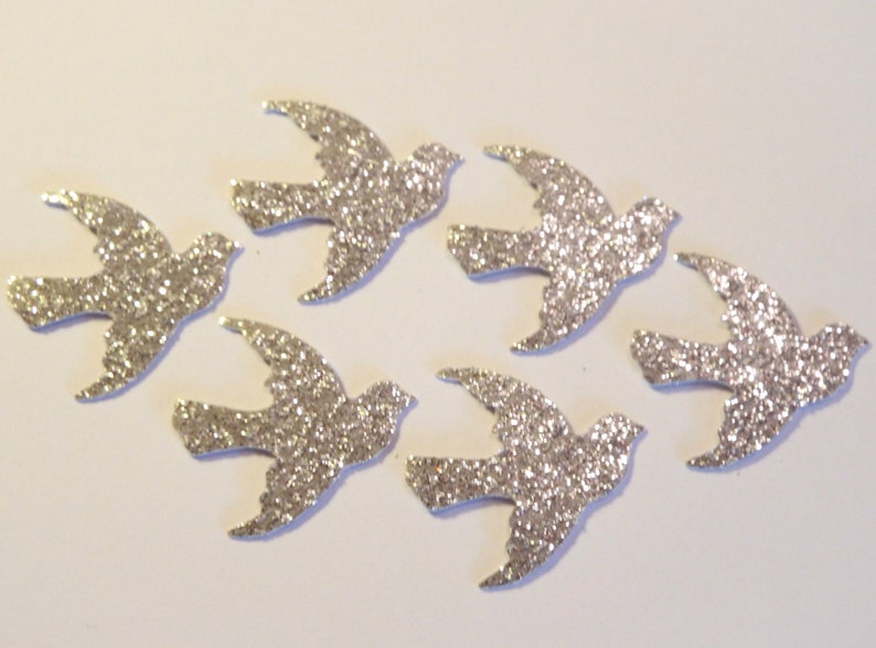 May include: Six silver glitter paper doves, each with a slightly different pose, are arranged on a white background.