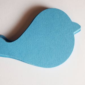 Op de afbeelding: Een stapel lichtblauwe papieren uitsparingen in de vorm van een vogel. Het silhouet van de vogel heeft een rond lichaam, een kleine puntige snavel en een staartgedeelte. Het papier heeft een matte textuur en een consistente, effen lichtblauwe kleur.