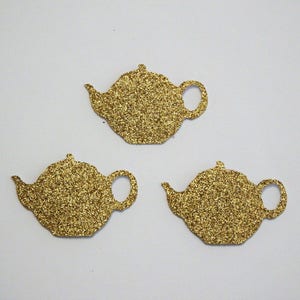 Peut inclure: Trois théières en paillettes dorées, chacune avec un design différent. Les théières sont découpées dans du papier et ont une finition scintillante.