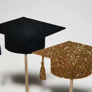 May include: Two graduation caps on sticks, one black and one gold glitter.
