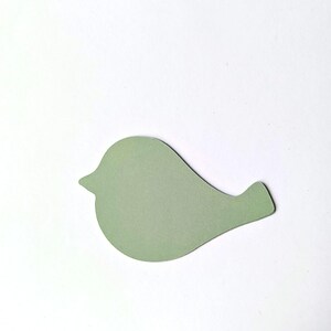 Op de afbeelding: Een platte, uitgestanste papieren vorm in de gedaante van een gestileerde vogel. Het vogel-silhouet is uitgevoerd in een effen, gedempte saliegroene kleur met een rond lichaam, een kleine puntige snavel en een korte, schuin aflopende staart.