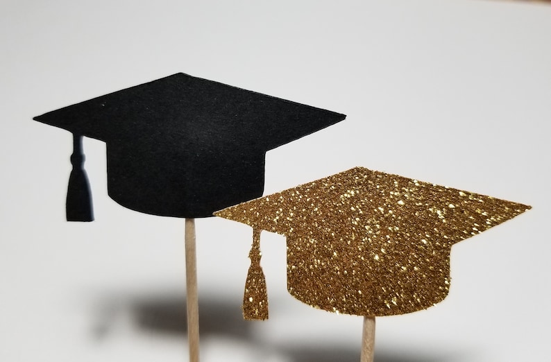 May include: Two graduation caps on sticks, one black and one gold glitter. The caps are perfect for decorating cupcakes or other treats for a graduation party.