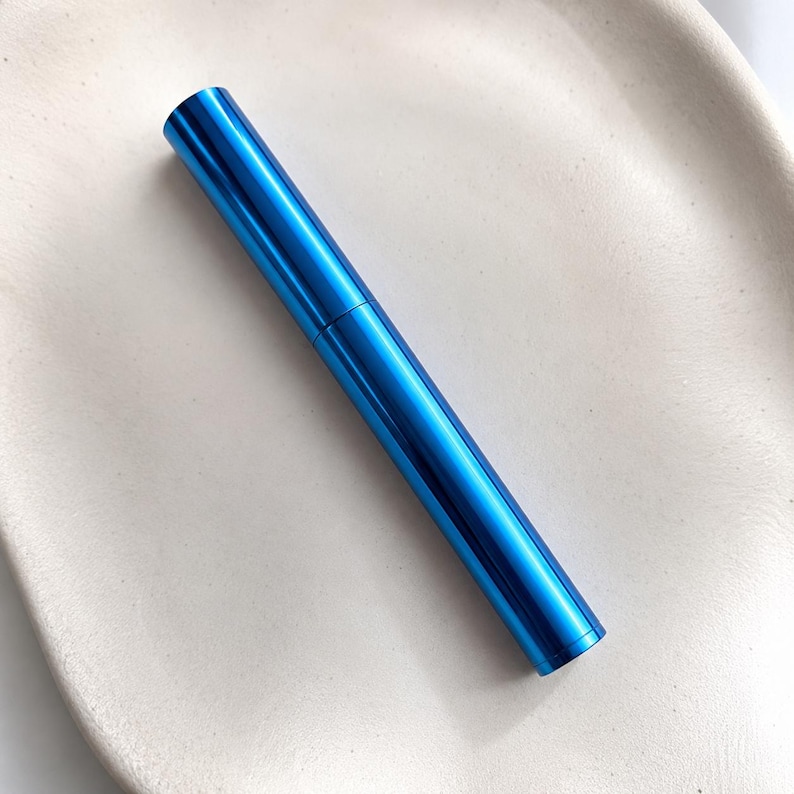May include: A cylindrical cosmetic tube with a vibrant, metallic blue finish. The item features a smooth, reflective surface and a straight, uniform shape, consisting of a main body and a matching cap that meet at a thin, horizontal seam line.