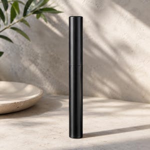 May include: A sleek, cylindrical black tube with a smooth matte finish. The object stands vertically and features a clean, minimalist design with a visible seam separating the cap from the main body, presenting a uniform and solid black color.