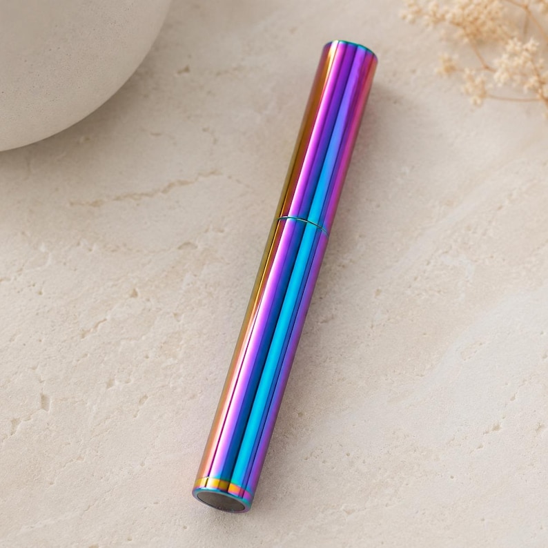 May include: A cylindrical metal tube with a vibrant iridescent finish that shifts between shades of blue, purple, and gold. The object features a smooth, reflective surface and a distinct horizontal seam separating the cap from the main body.